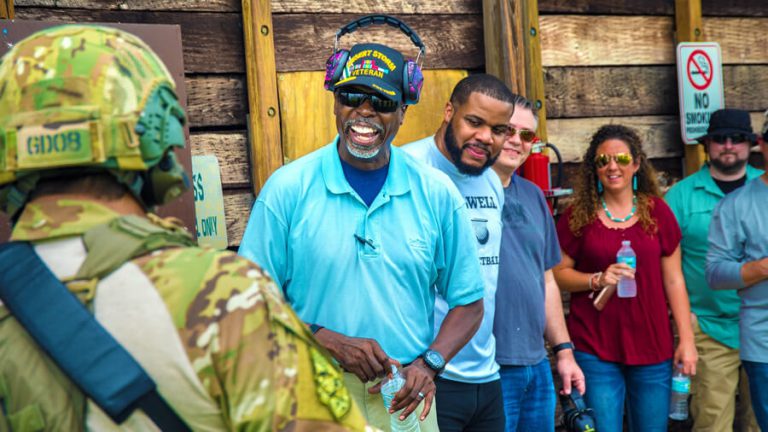 A group of FBI Citizens Academy members looking at a person standing in the foreground dressed in camouflage. The person's back is to the camera, and the group is laughing and smiling.